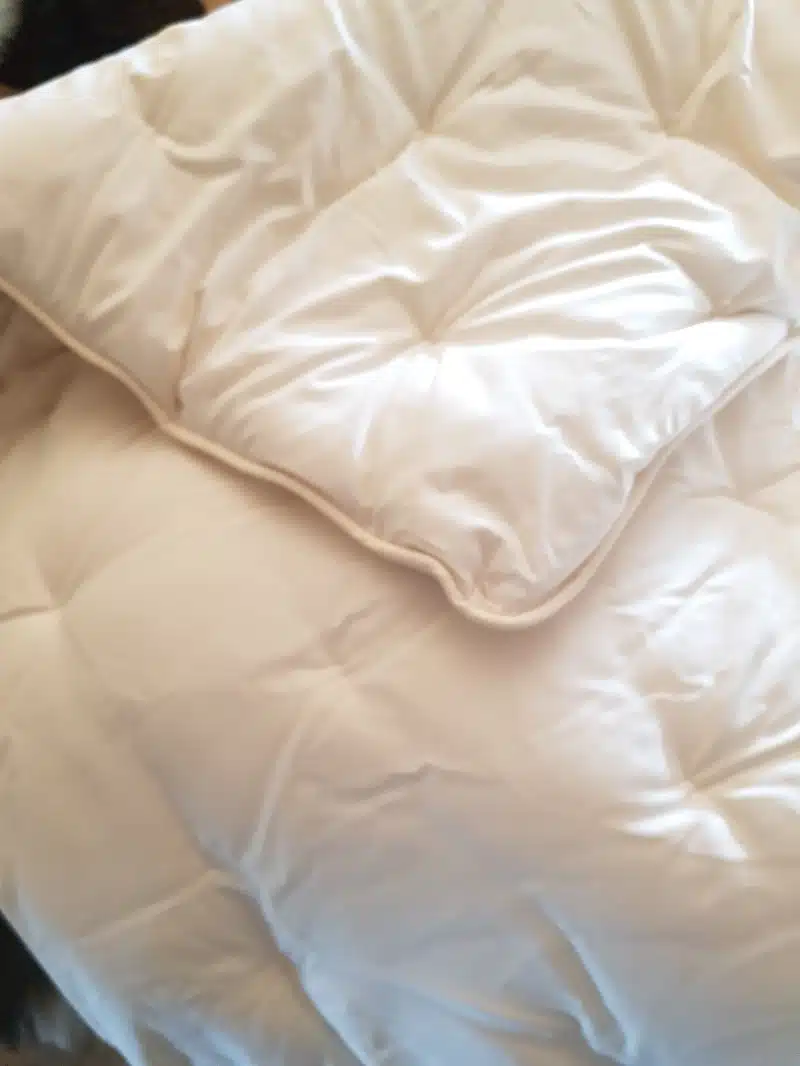 Weiße Steppdecke mit Karosteppung und abgerundeter Kante liegt auf einem Bett