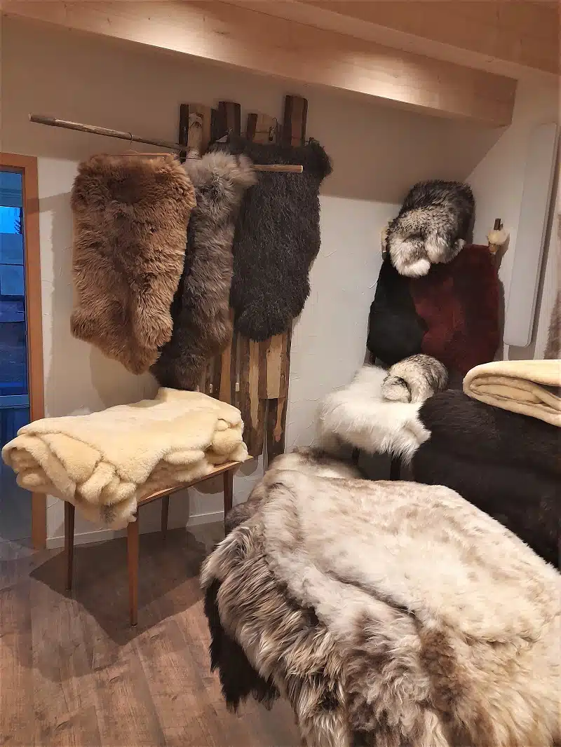 Verschiedene Schaffelle in Braun, Grau und Weiß hängen an einer Holzwand und liegen auf einem Tisch.